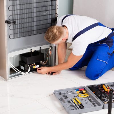 Young Male Technician Checking Refrigerator With Screwdriver